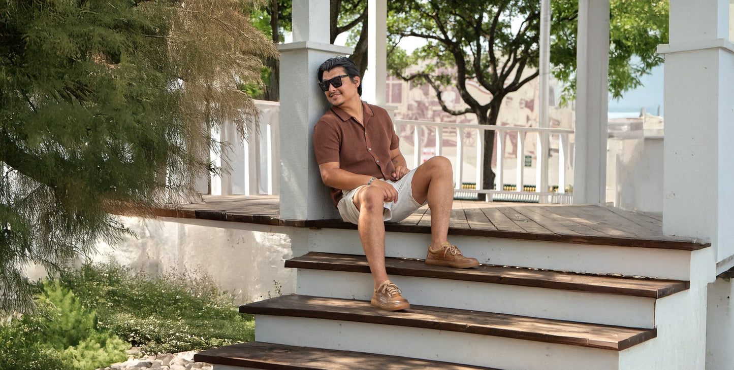A person in dark jeans and black sneakers with tan soles leans against a brick wall.