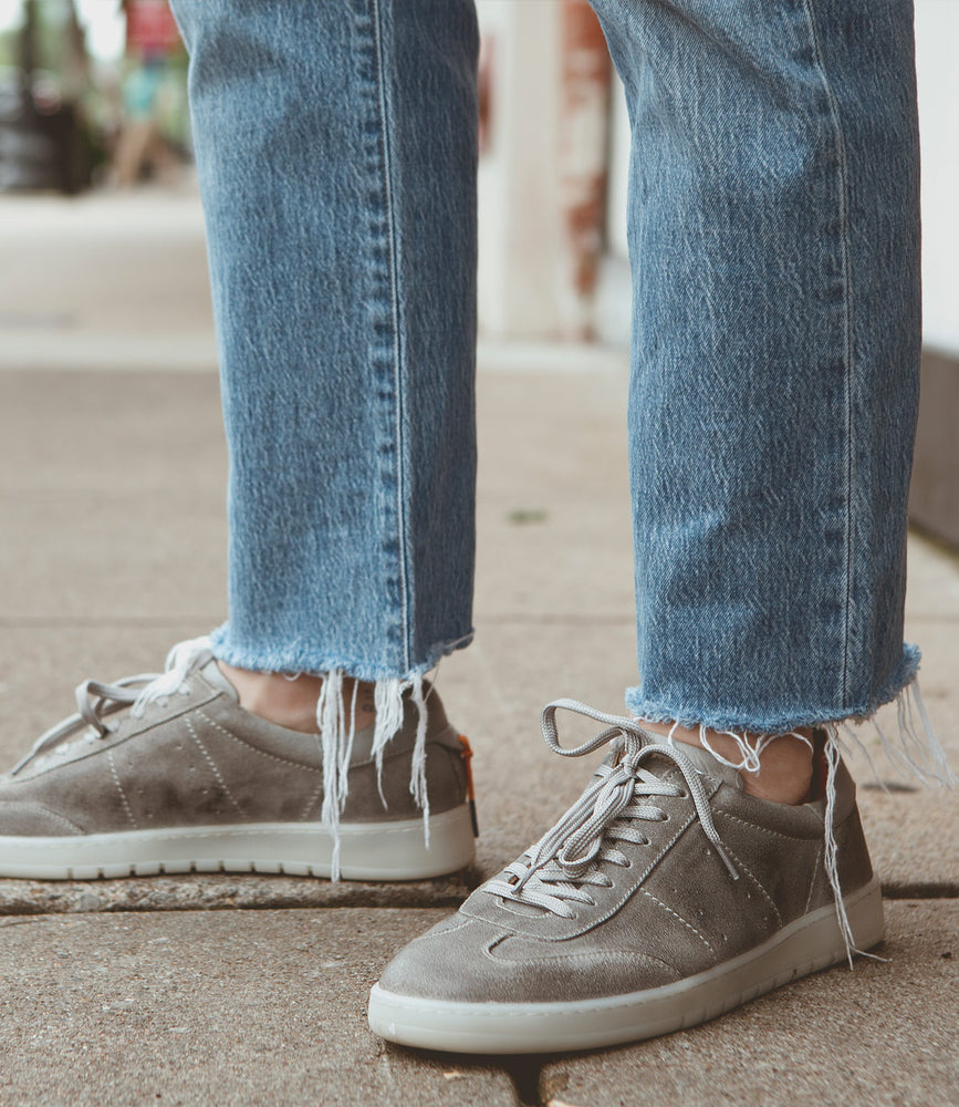 
                  
                    A person wearing frayed hem jeans and gray Roan Attitude sneakers with a suede leather upper stands on a sidewalk.
                  
                