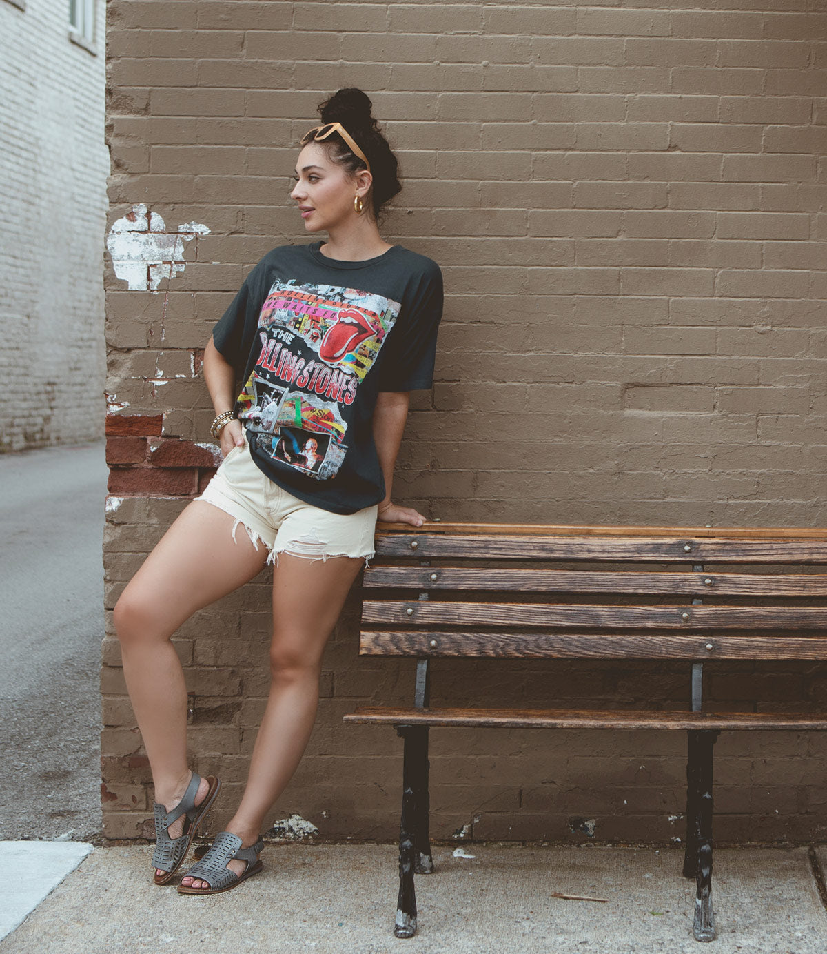 
                  
                    Woman wearing denim shorts and a band t-shirt leans against a brick wall next to a wooden bench, her Roan Ballad II boots featuring resilient rubber heels.
                  
                
