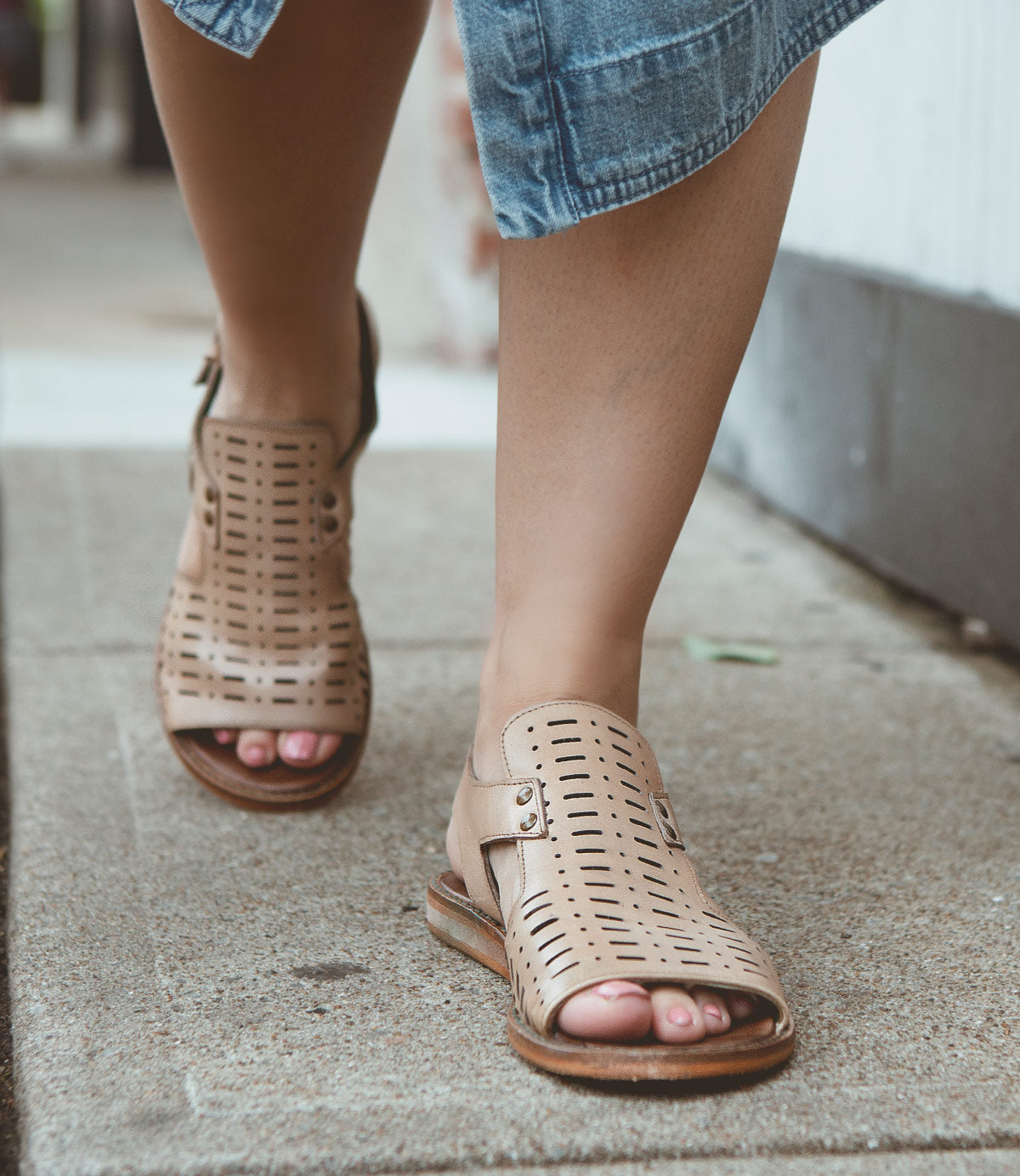 
                  
                    Close-up of a person wearing Roan Ballad II tan, full-grain leather sandals with an adjustable ankle closure and a blue skirt while walking on a sidewalk.
                  
                