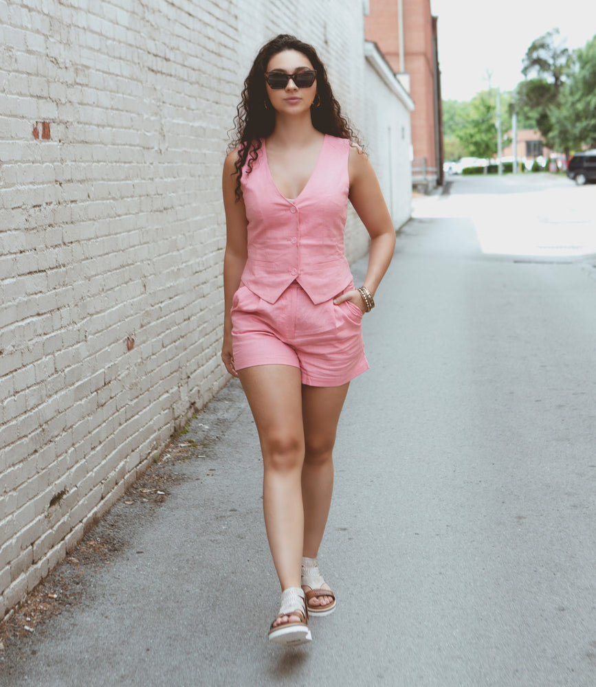 
                  
                    A woman in a pink vest and shorts, sunglasses, and Roan Carlita II sandals with a comfortable footbed walks down an alley with brick walls.
                  
                