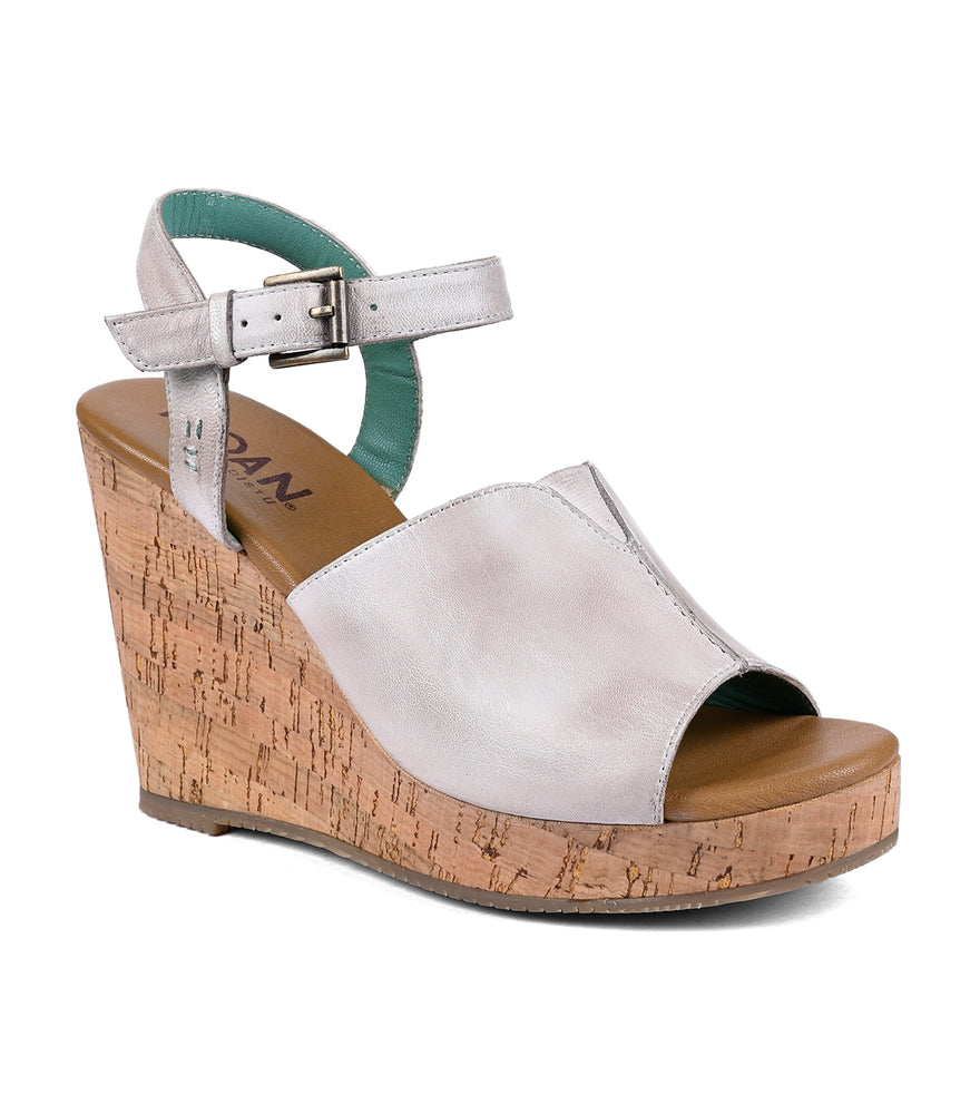 Silver open-toe wedge sandal with a cork heel and a flexible fit ankle strap, isolated on a white background by Roan Deduction.