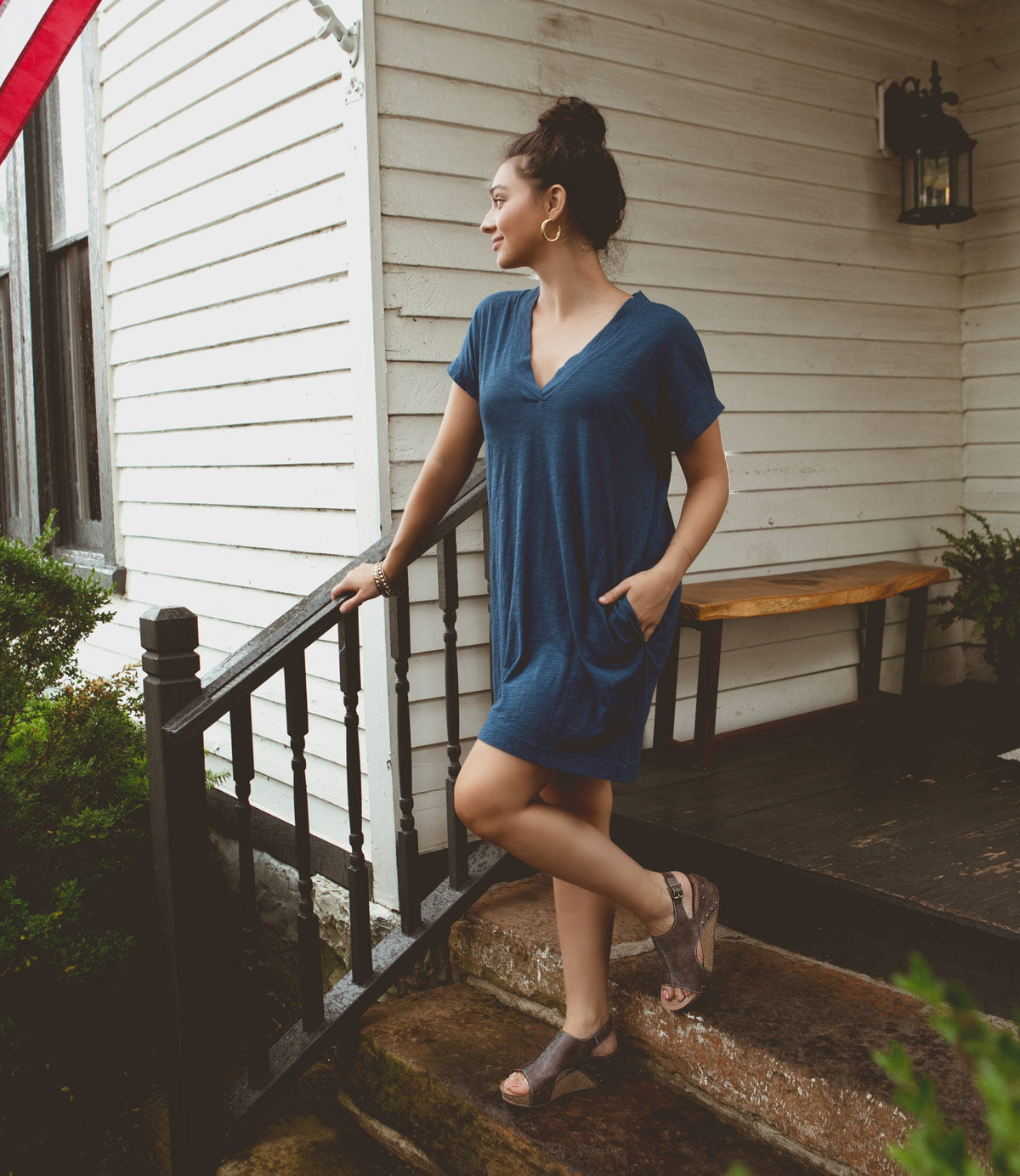 
                  
                    A woman in a blue dress stands outside on a porch, leaning on the railing and looking to the side, effortlessly showcasing her Roan Fortnight shoes that promise all-day comfort.
                  
                