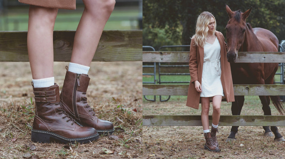 A person in a white dress and brown coat stands by a horse near a wooden fence. Close-up of brown lace-up boots on the left.