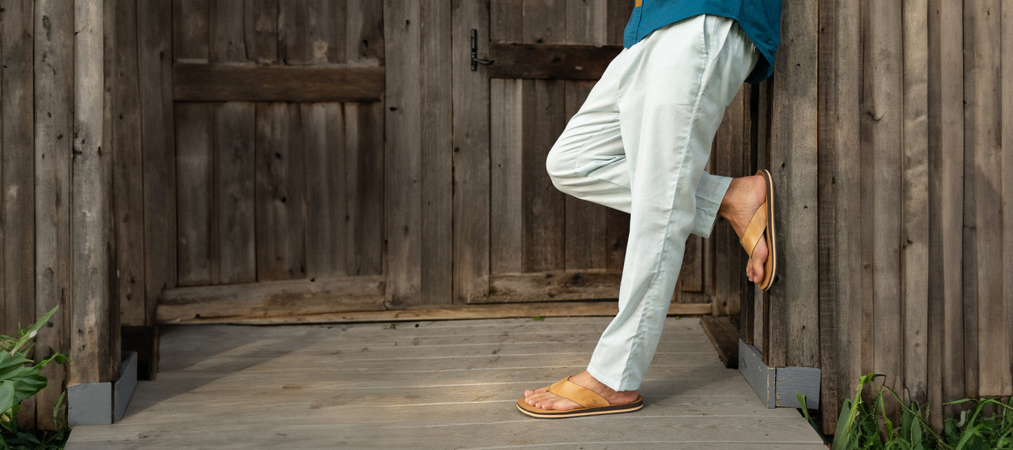 A pair of gray slip-on shoes placed on top of a pile of firewood against a wooden wall.