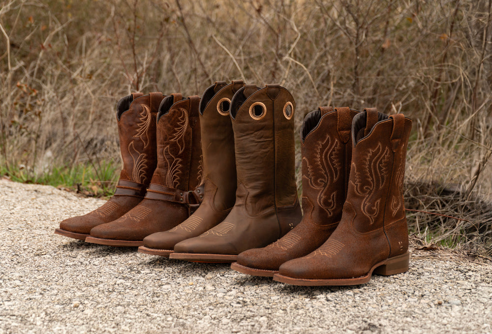 Close up of brown boots with blue jeans standing on grass.