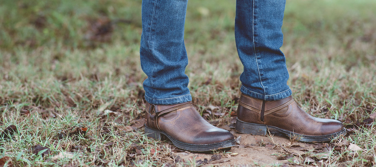 Close up of brown boots with blue jeans standing on grass.