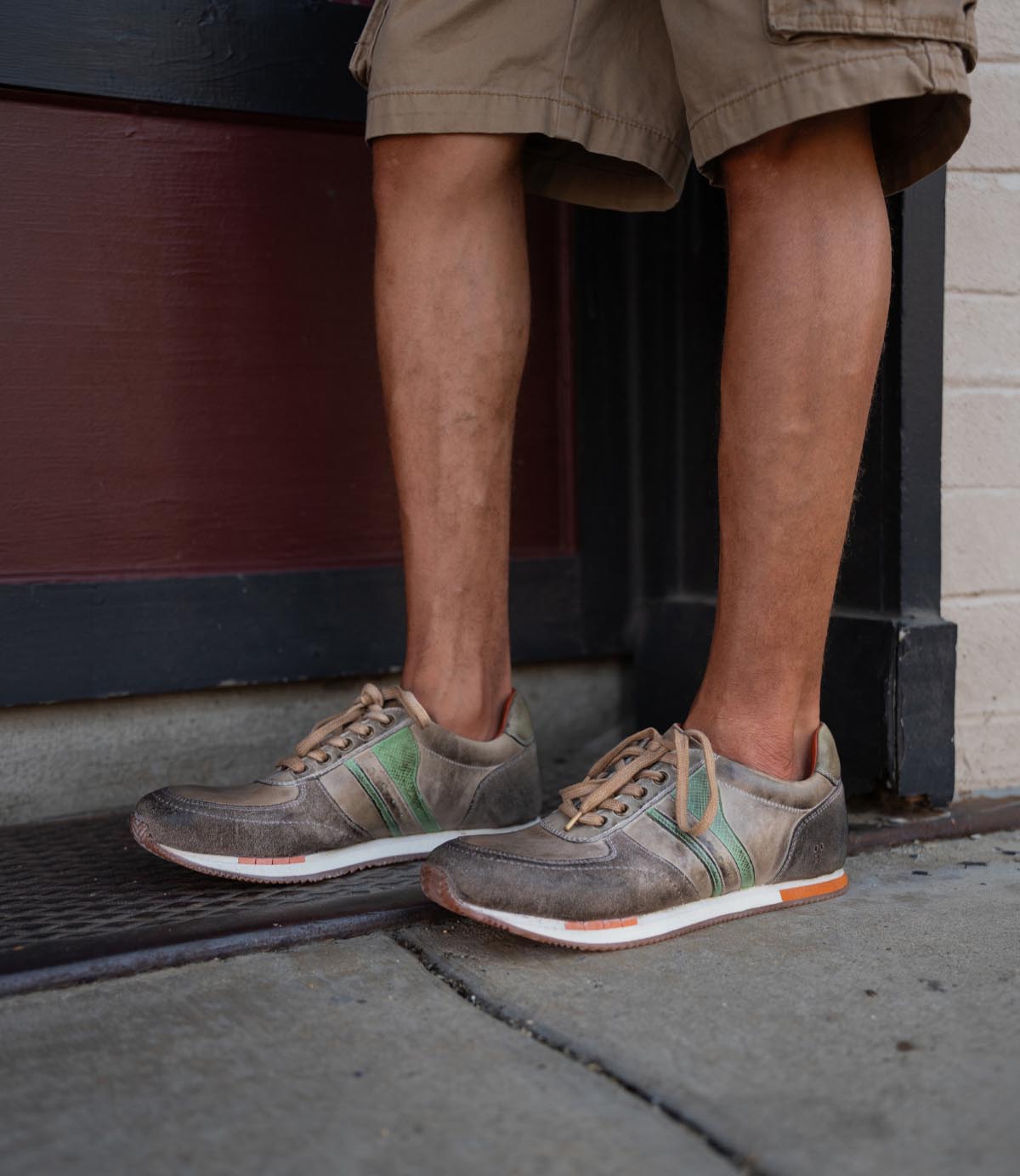 Wearing Roan's Into distressed denim shorts and platform jute sandals with cushioned soles, a person stands against a textured brick wall.