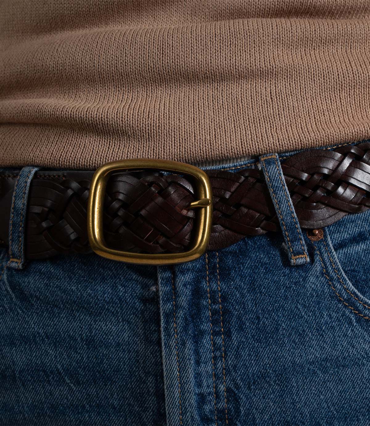 
                  
                    A person wearing blue jeans, a tan knit top, and the Roan Alder dark brown braided leather belt with a large rounded metal buckle.
                  
                