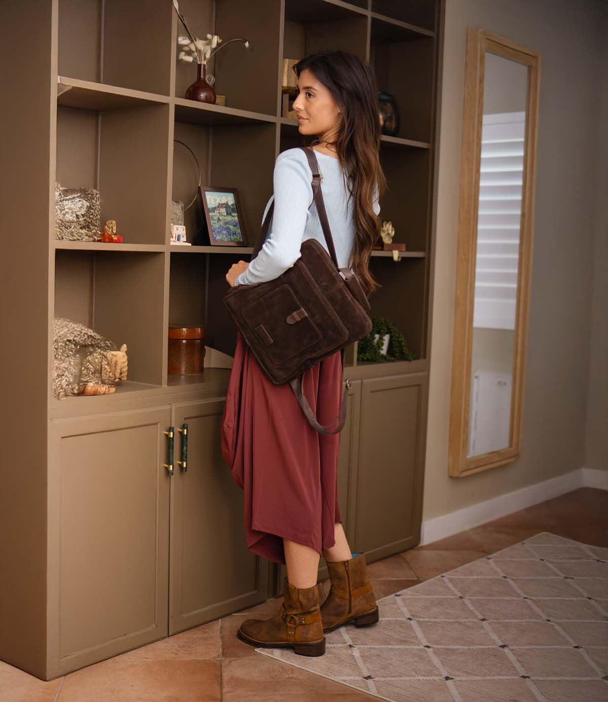 
                  
                    A person wearing a long skirt and brown boots carries a dark brown suede Roan Yearling crossbody bag with leather straps.
                  
                