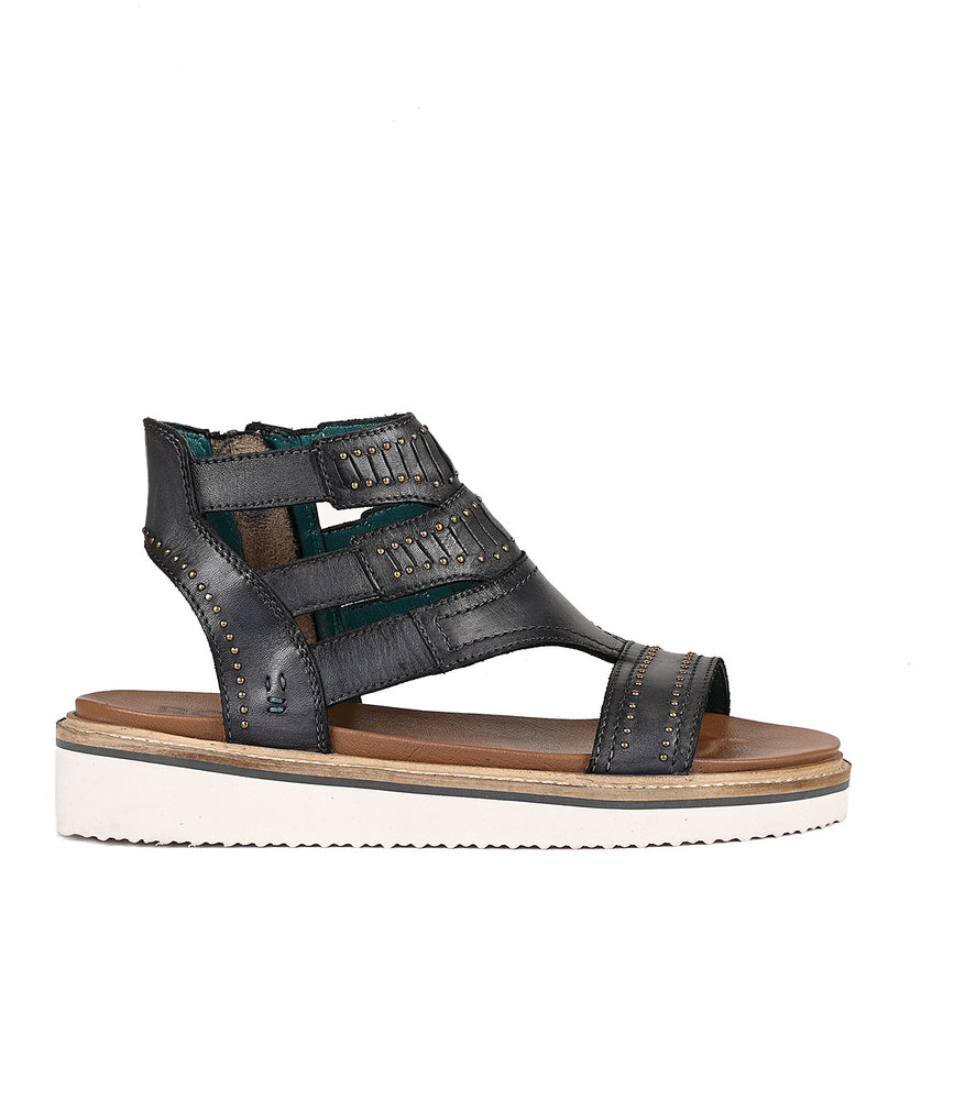
                  
                    Carlita II black full-grain leather strappy sandal with studs on a white background by Roan.
                  
                