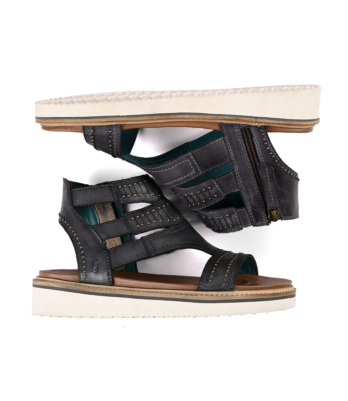 
                  
                    Black full-grain leather Carlita II gladiator sandals by Roan displayed with one shoe positioned upright and the other placed flat, showing soles.
                  
                