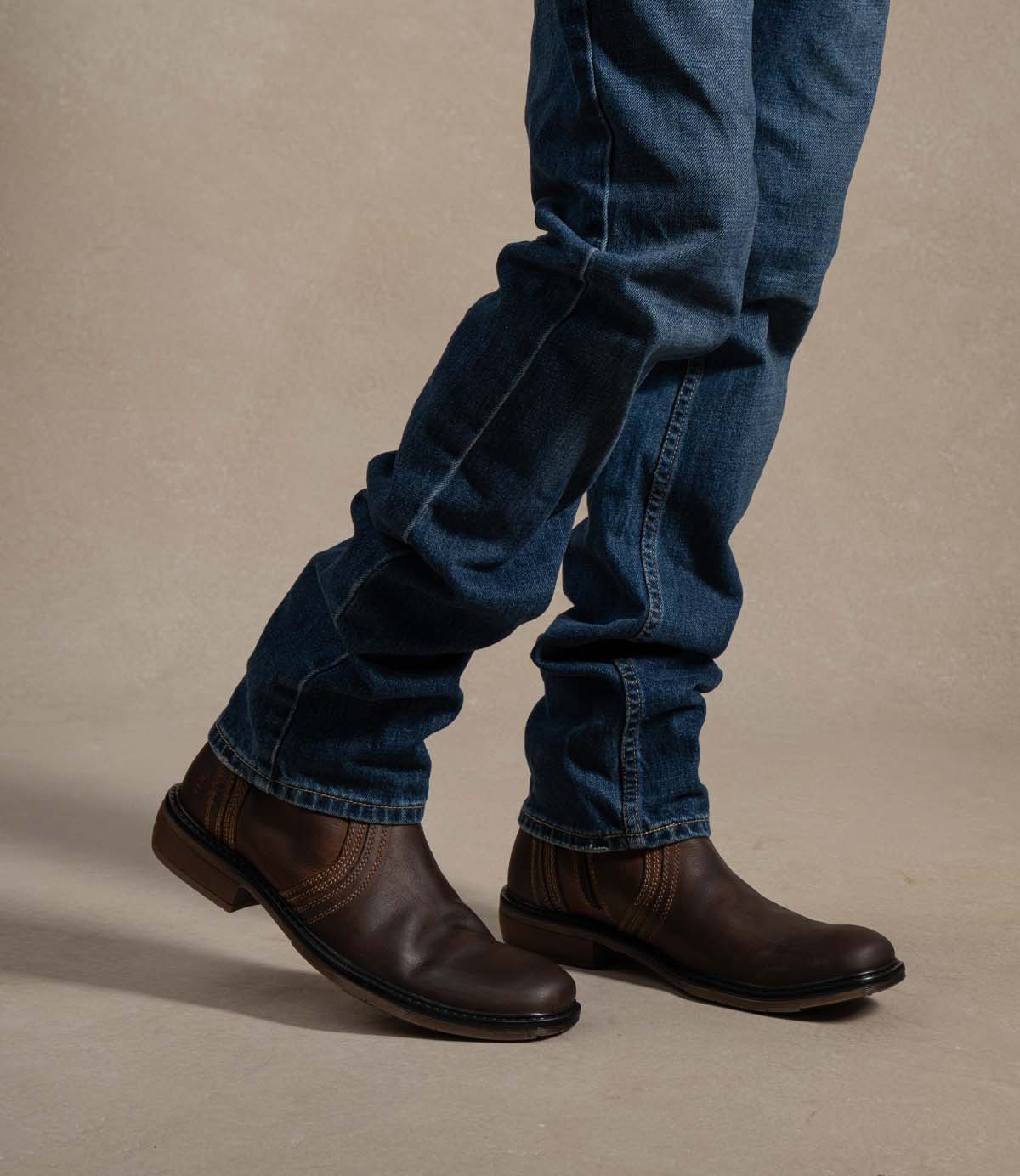 
                  
                    A person wearing blue jeans and the Roan Crestone boot, featuring a sturdy rubber sole, stands on a beige surface.
                  
                