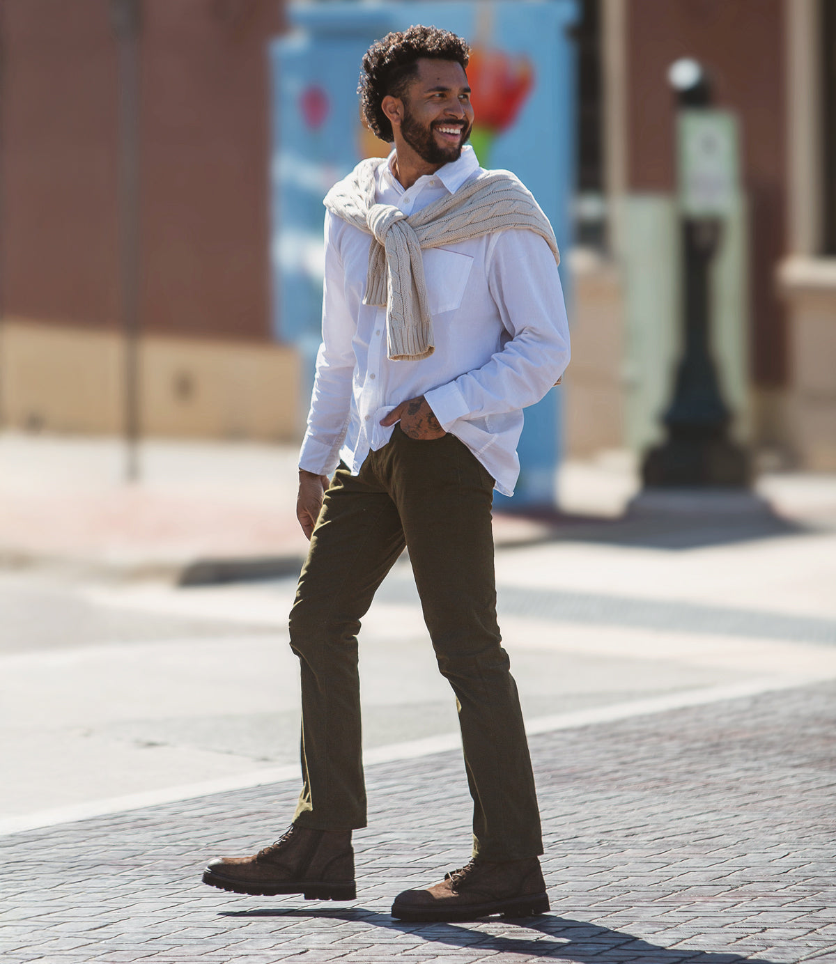 
                  
                    A man walks confidently on a sunny street, wearing a white shirt, sweater over his shoulders, olive pants, and brown Duty suede boots by Roan with a convenient side zipper.
                  
                
