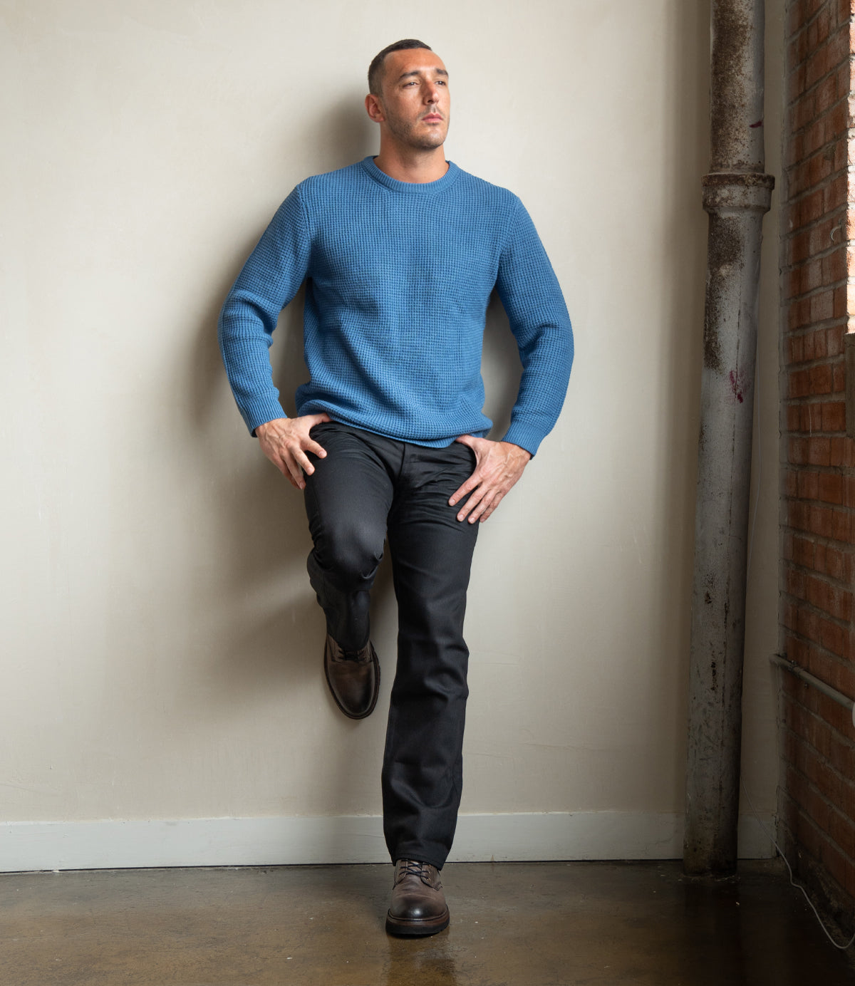 
                  
                    A man leans indoors against a wall in dark pants and a blue sweater, one knee raised, highlighting Roan’s Duty boots—stylish men’s footwear featuring a comfortable padded insole.
                  
                