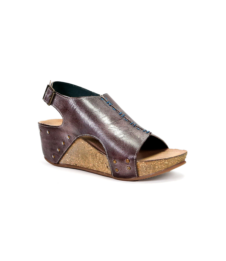 
                  
                    A metallic burgundy platform style wedge sandal with cork heel and peep toe, featuring rivet details and a buckle ankle strap, isolated on white background by Roan Fortnight.
                  
                