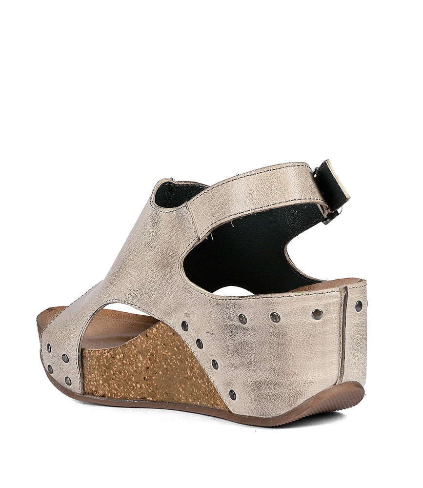 
                  
                    A beige full-grain leather wedge sandal with a cork heel, studded details, and an ankle strap, isolated on a white background by Roan Fortnight.
                  
                