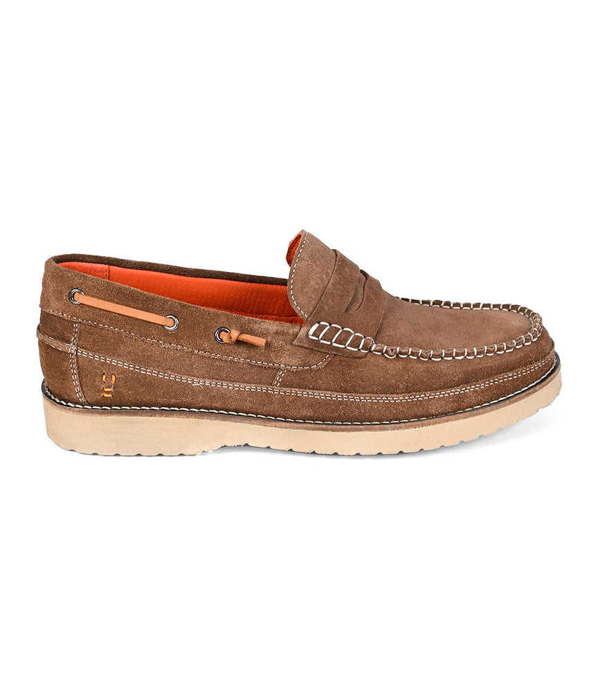 The Roan Grid is a brown suede penny loafer with white stitching, side lace detail, orange inner lining, cushioned insole, and a beige rubber sole. Shown here in side profile.