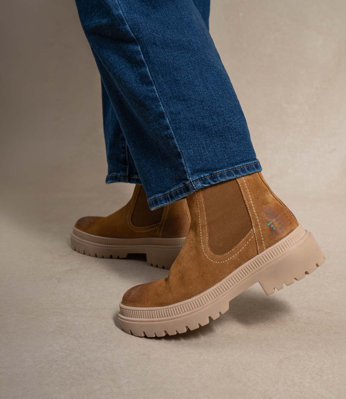 Person wearing blue jeans and the Roan Indwelt slip-on chunky suede Chelsea boots with a thick beige platform sole, standing on a neutral background.
