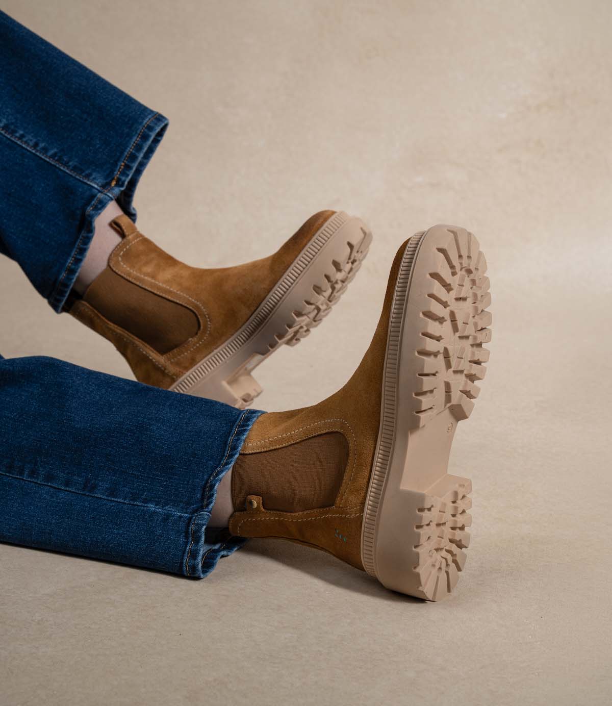 
                  
                    A person wearing Roan’s Indwelt tan chunky suede Chelsea boots with a platform sole and blue jeans, showcasing the tread pattern of these slip-on boots.
                  
                