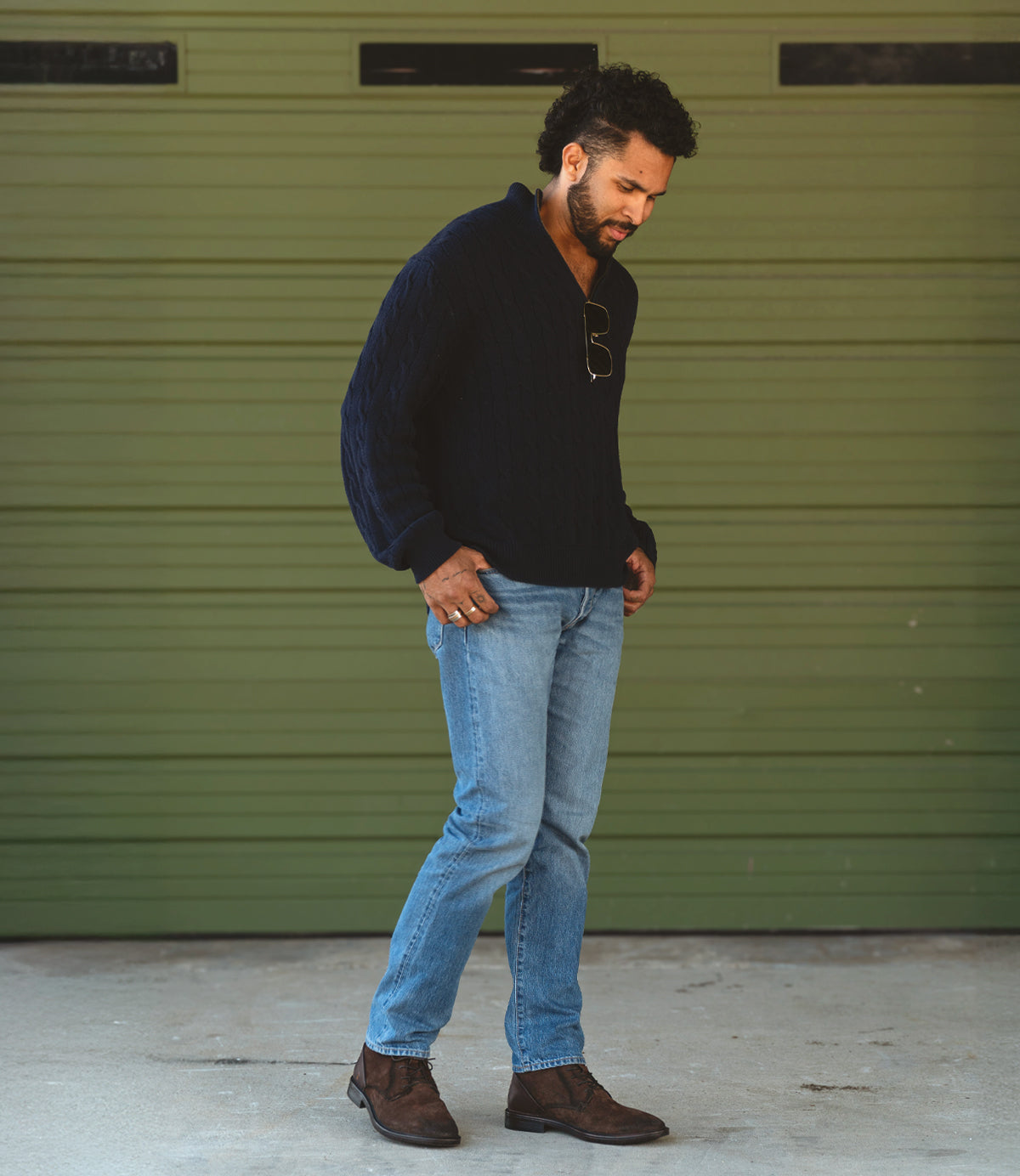 
                  
                    A man, wearing a dark sweater, light blue jeans, and Roan's rugged Joyride lace-up boots, stands confidently in front of a green garage door.
                  
                
