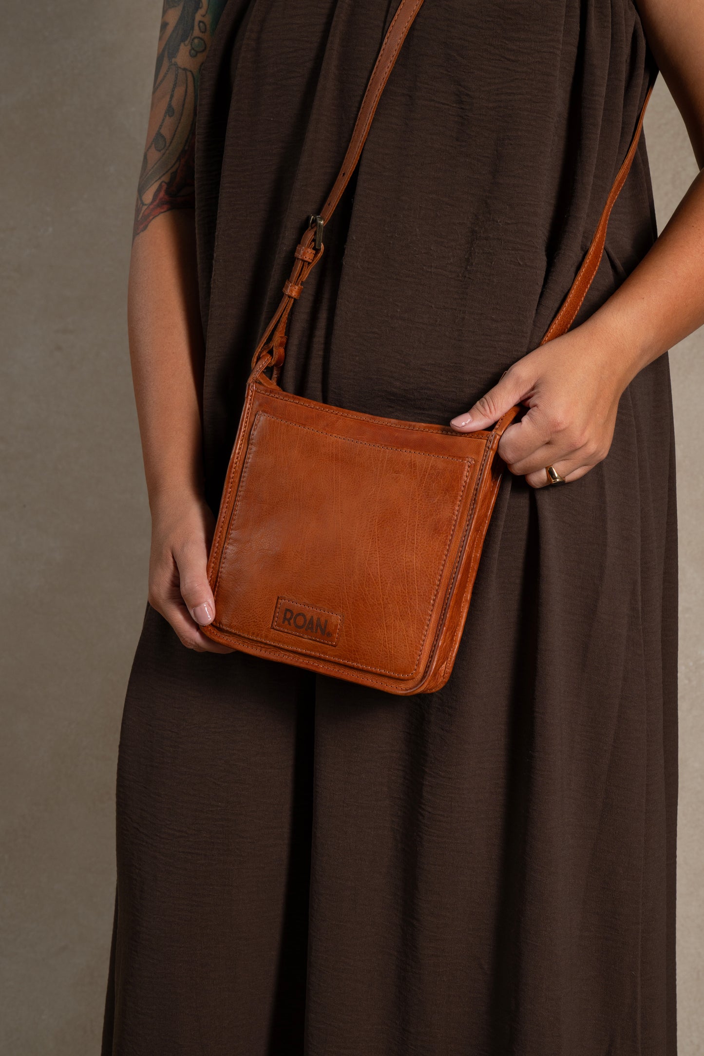 
                  
                    A person in a brown dress holds the Quetzal, a small brown leather crossbody bag from ROAN featuring an embossed logo, adjustable strap, and secure zip closure, designed for everyday use.
                  
                