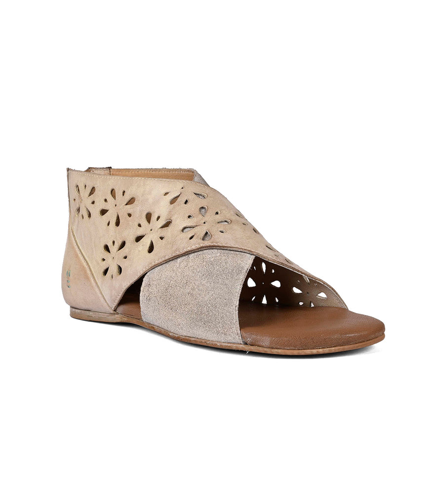 A beige suede women's ankle boot with a laser-cut floral design, featuring a peep toe and a low heel, isolated on a white background by Roan Rotation.
