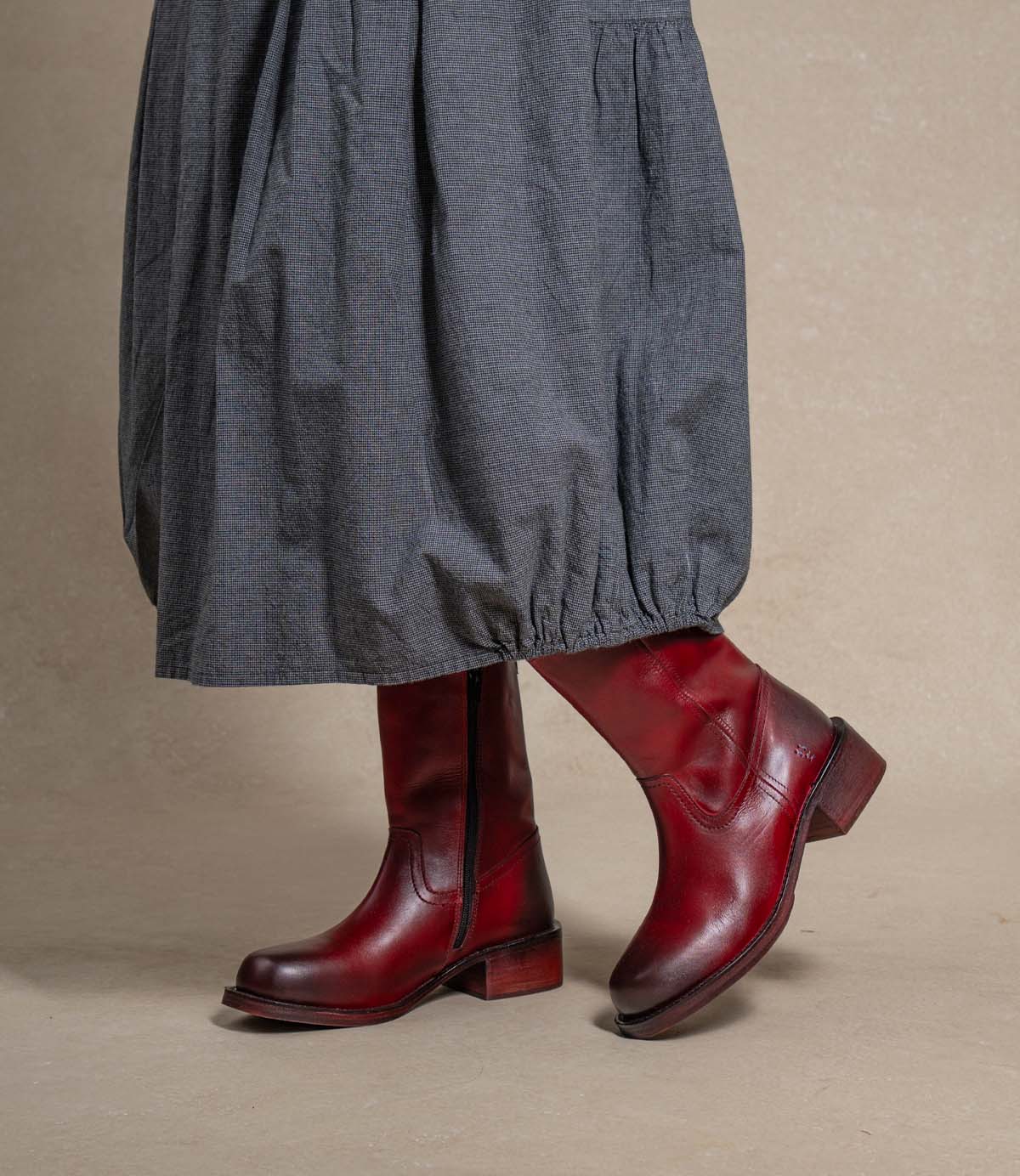 
                  
                    A person wearing the Roan Splitter boots—dark red, sturdy footwear featuring a chunky leather silhouette and an inner-ankle zipper—stands on a neutral background with a gray, ankle-length skirt.
                  
                