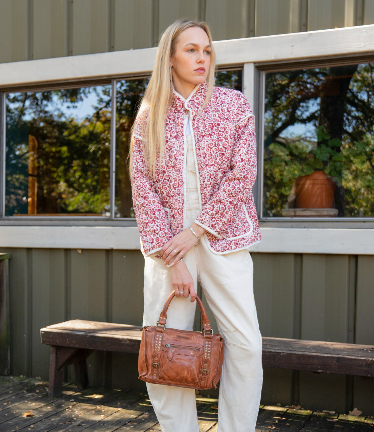 
                  
                    A woman stands outside a building wearing Roan’s Visual white outfit paired with a red patterned jacket and carrying a brown leather satchel.
                  
                