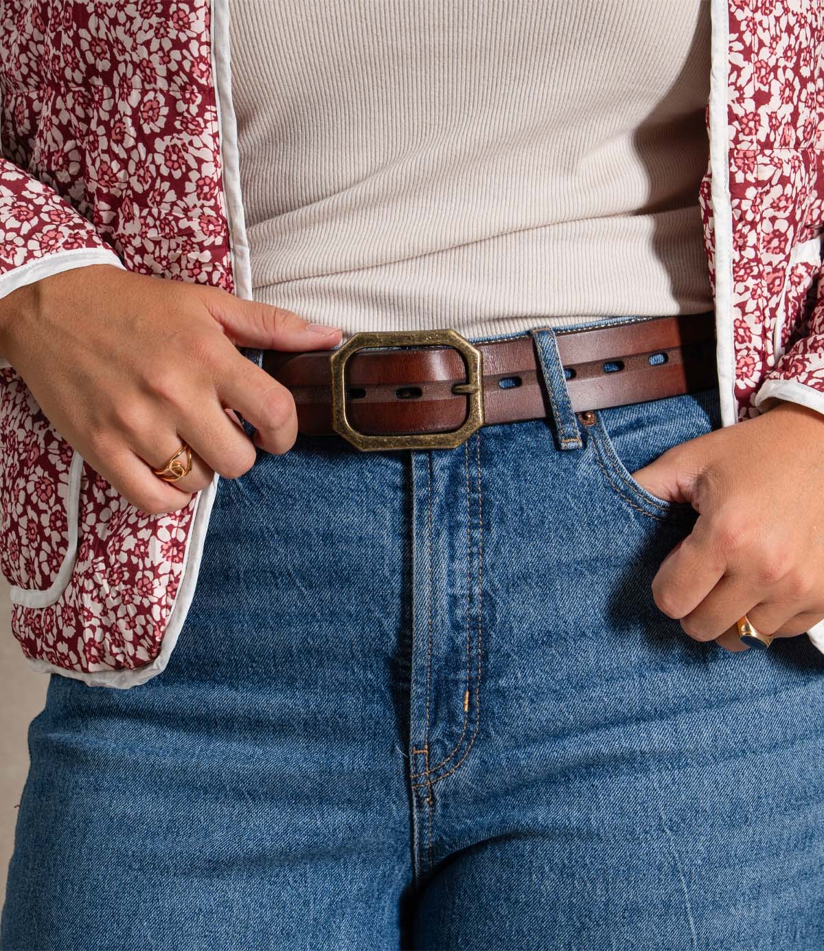 
                  
                    A person wearing the Roan Waymark floral red and white jacket, a beige ribbed top, blue jeans, and a brown belt with stitched edges and a large square buckle.
                  
                