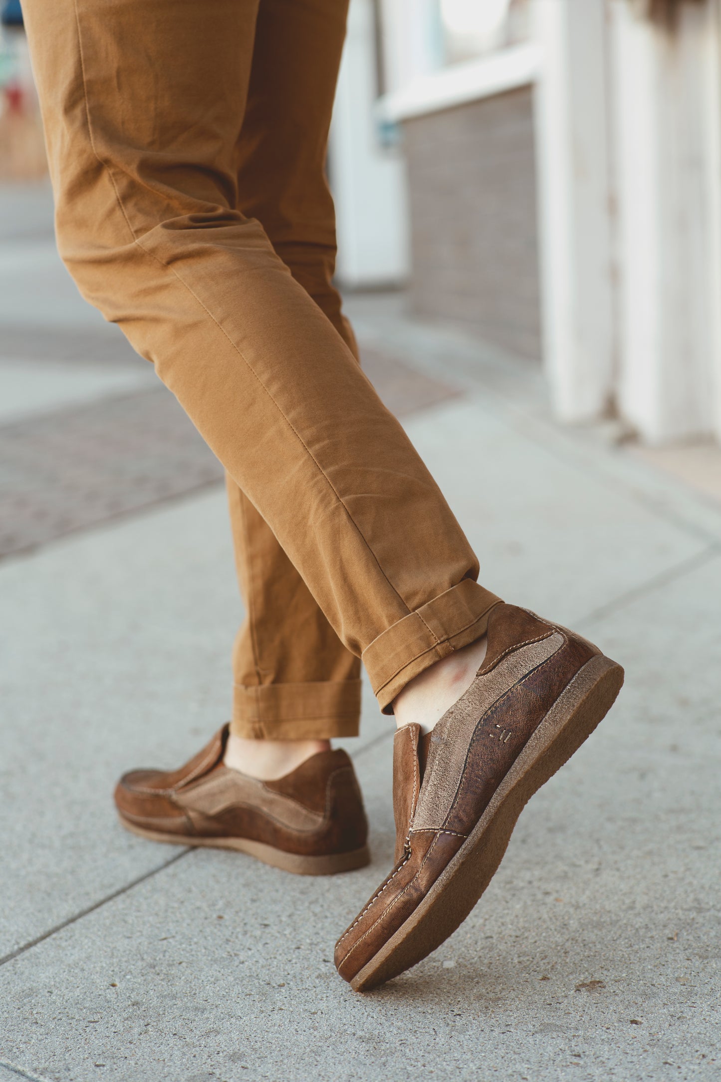 Person wearing Roan Shevon brown leather slip-on shoes with matching trousers on a sidewalk.